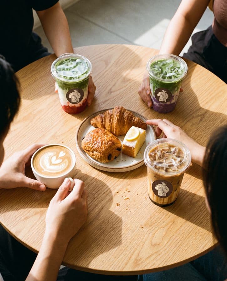 Friends' hands around a café table with four Hada drinks and pastries