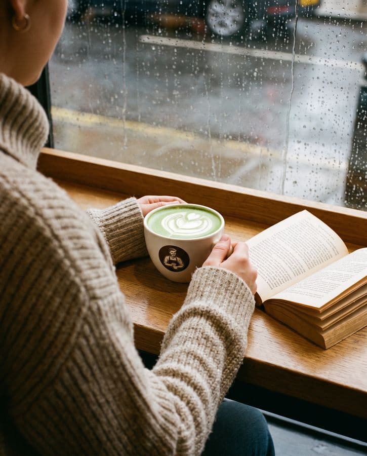 A hot matcha latte and an open book at a rainy window